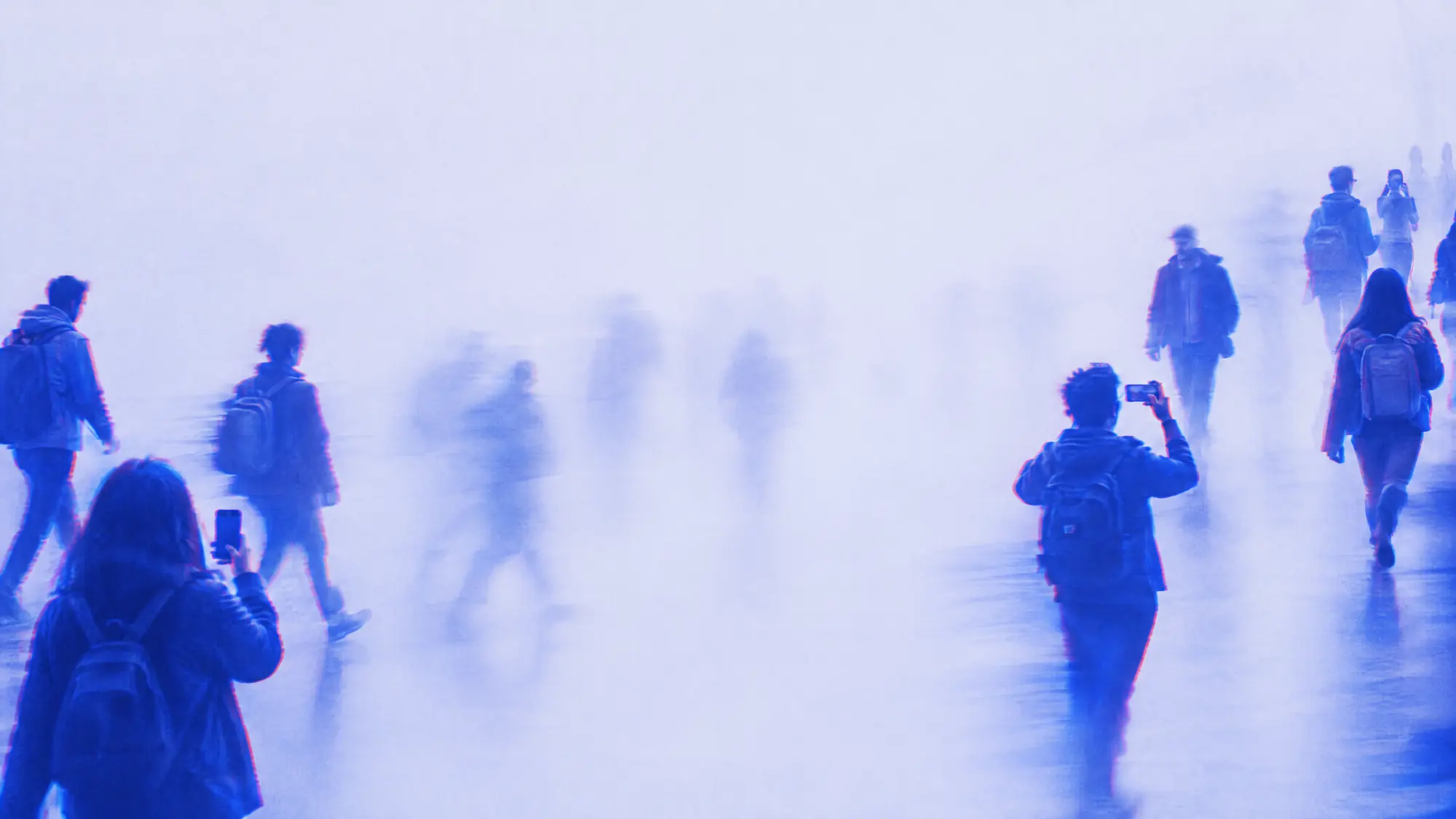 Personas caminando con sus celulares entre niebla azul